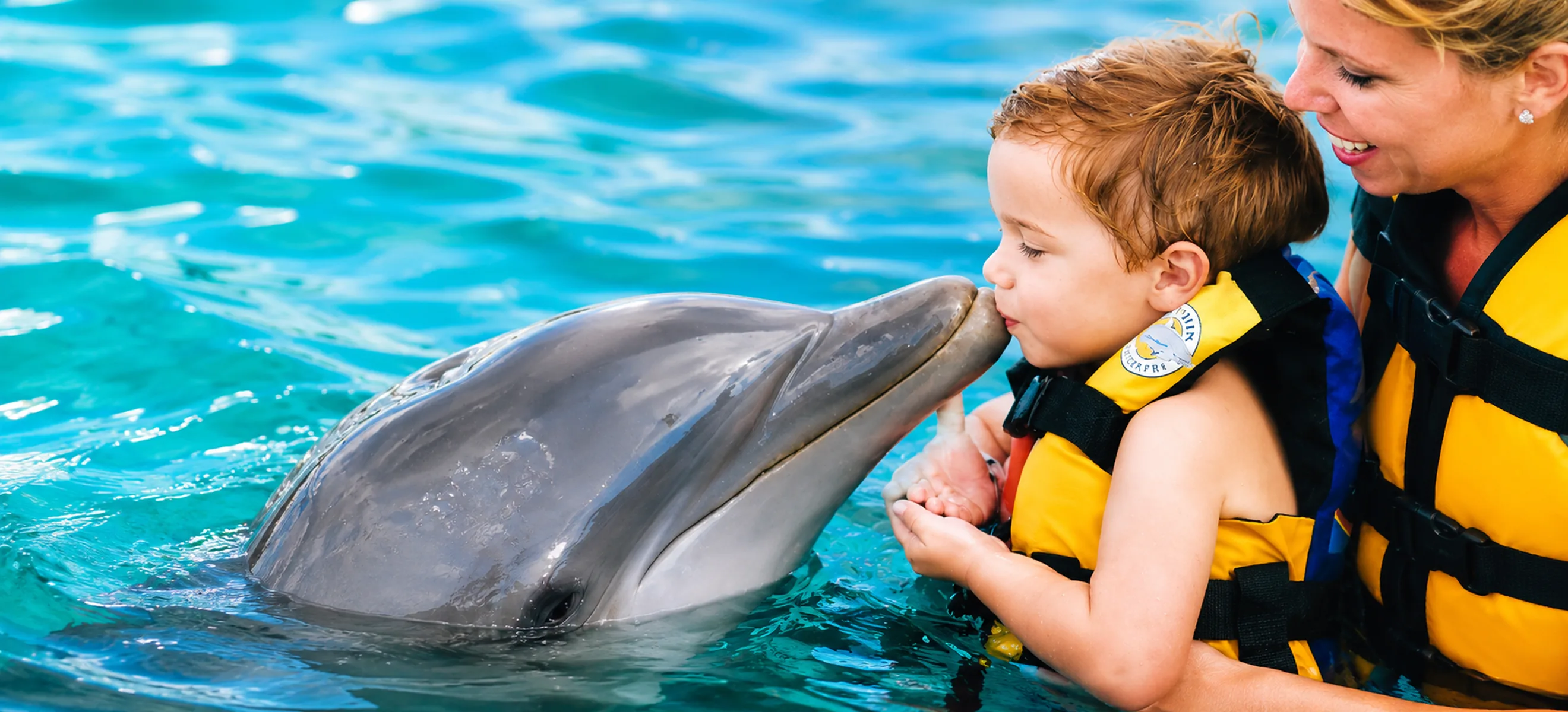 Young child enjoying a gentle dolphin kiss with an adult during the Dolphin Funtastic experience in Punta Cana, Dominican Republic.