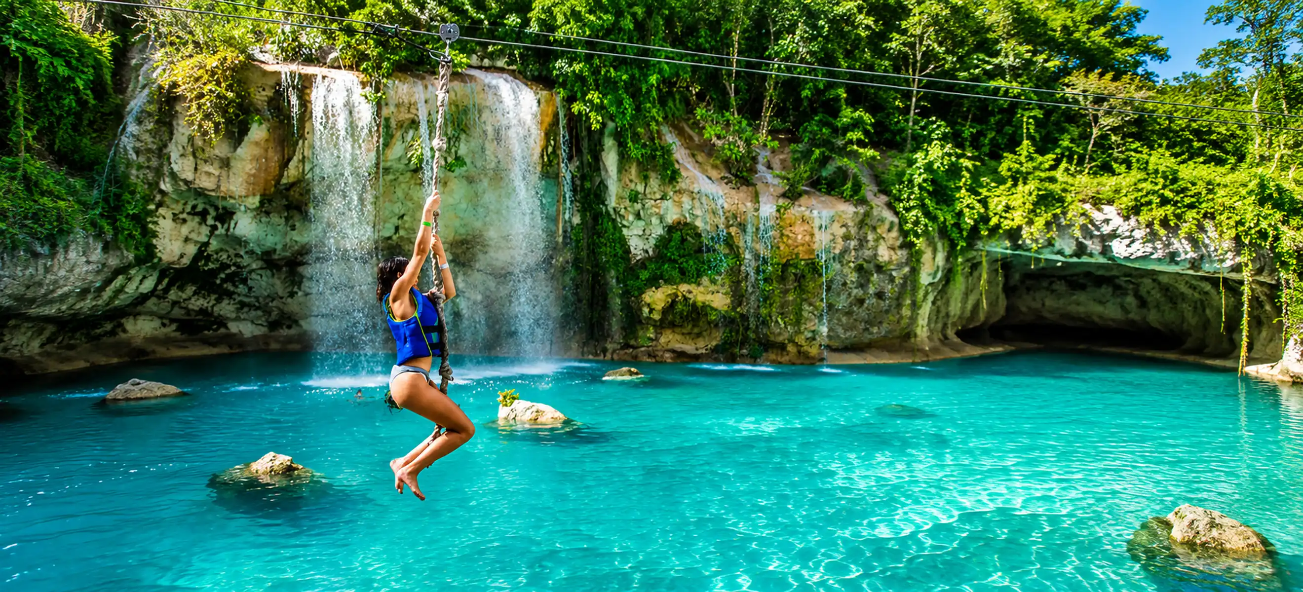 	Guest enjoying the rope swing over a crystal-clear turquoise lagoon surrounded by waterfalls at Scape Park Cap Cana in Punta Cana, Dominican Republic.
