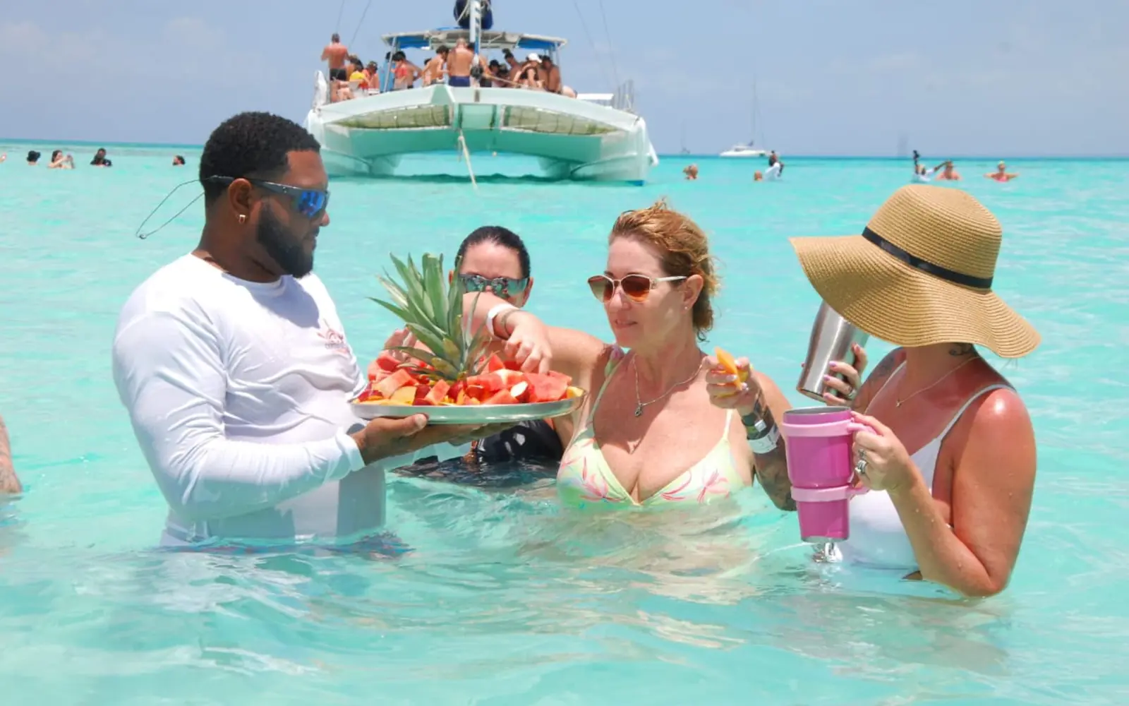 Guests enjoying tropical fruit and drinks in the turquoise natural pool during a private Saona Island catamaran excursion