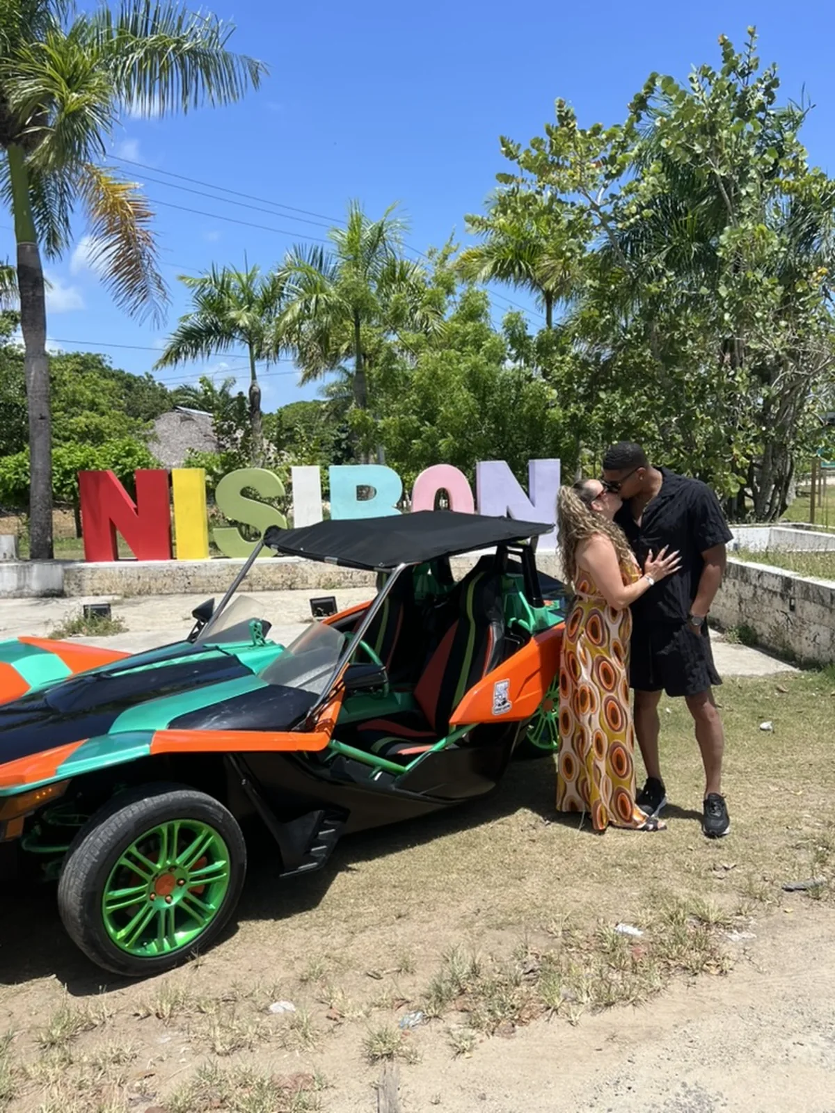Couple celebrating beside a colorful Polaris Slingshot at the Nisibón Sign